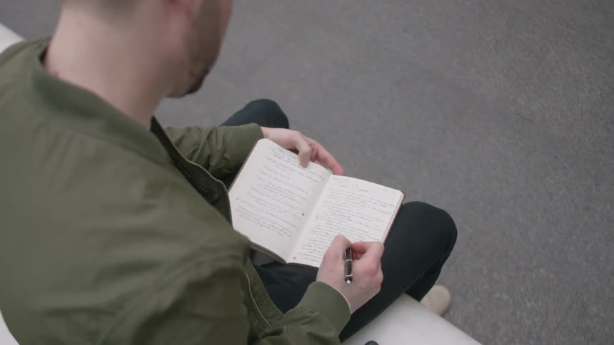 A man is sitting down writing in his notebook