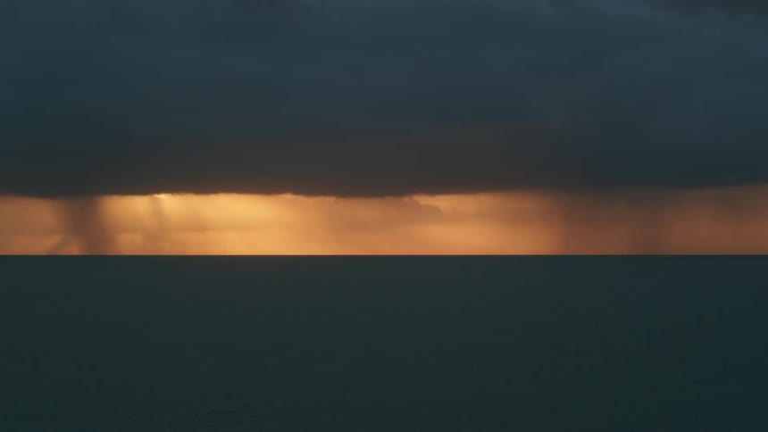Rain is falling from clouds on the horizon at sunset