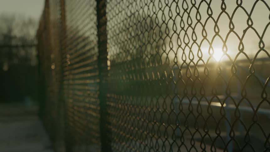 The sun is setting behind the chain link fence