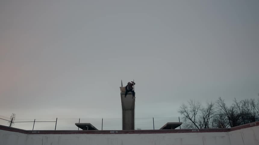Man sits on a diving board over an empty swimming pool
