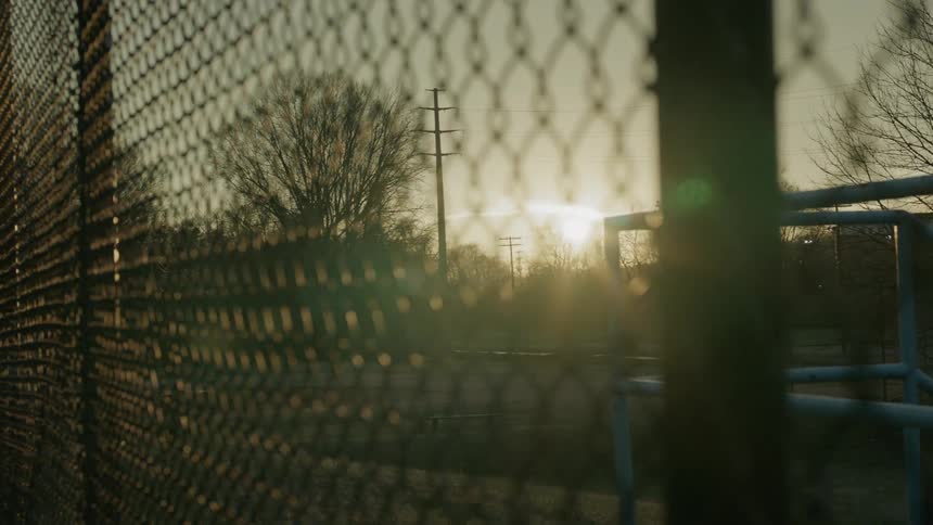 The sun shines through the chain link fence