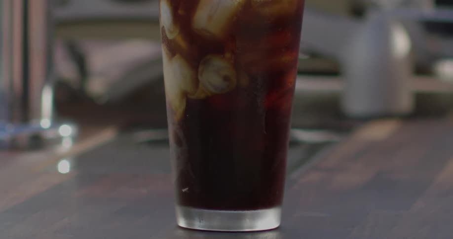 Cream is mixing into an iced beverage inside in daylight