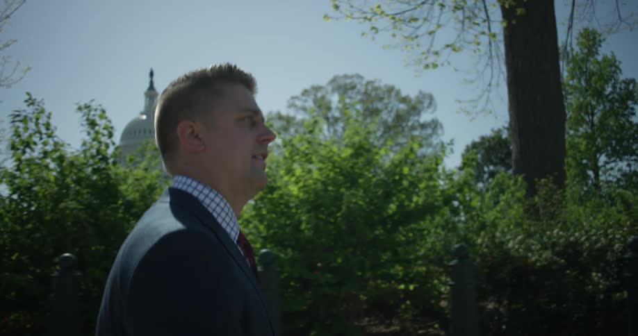 Man in a suit walks near the trees
