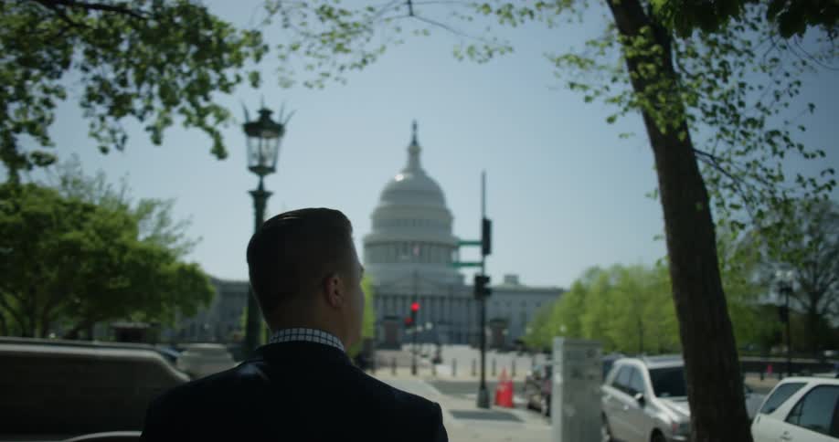 A man is walking towards a capitol building outside on a sunny day