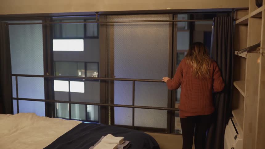 A young woman walks to the hotel room window to look outside