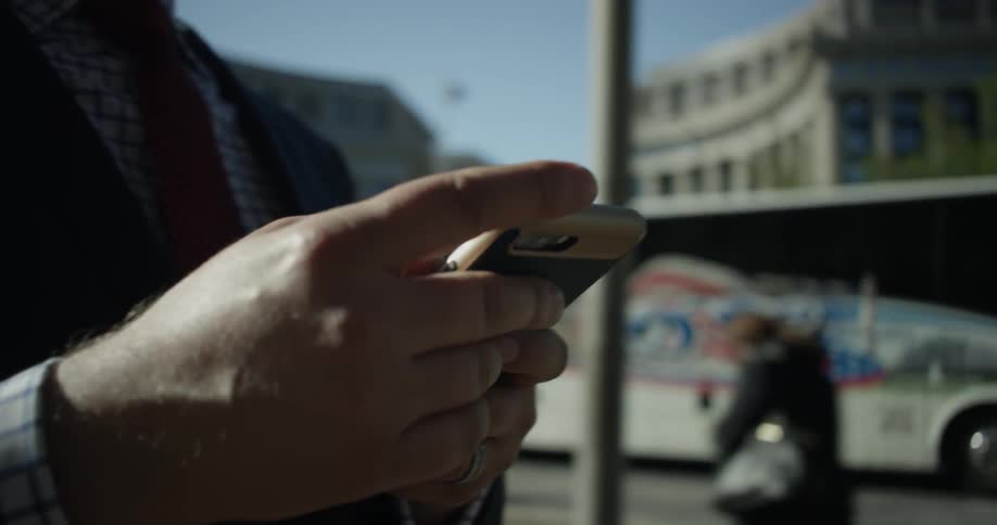 A man is using his phone as a bus passes