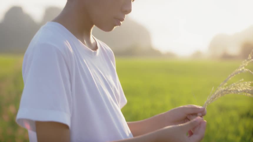 A child is holding grass near some flowers