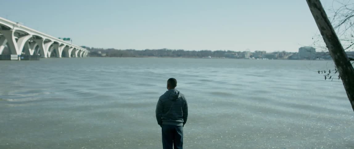 A man is looking across a river in an urban area on a sunny day