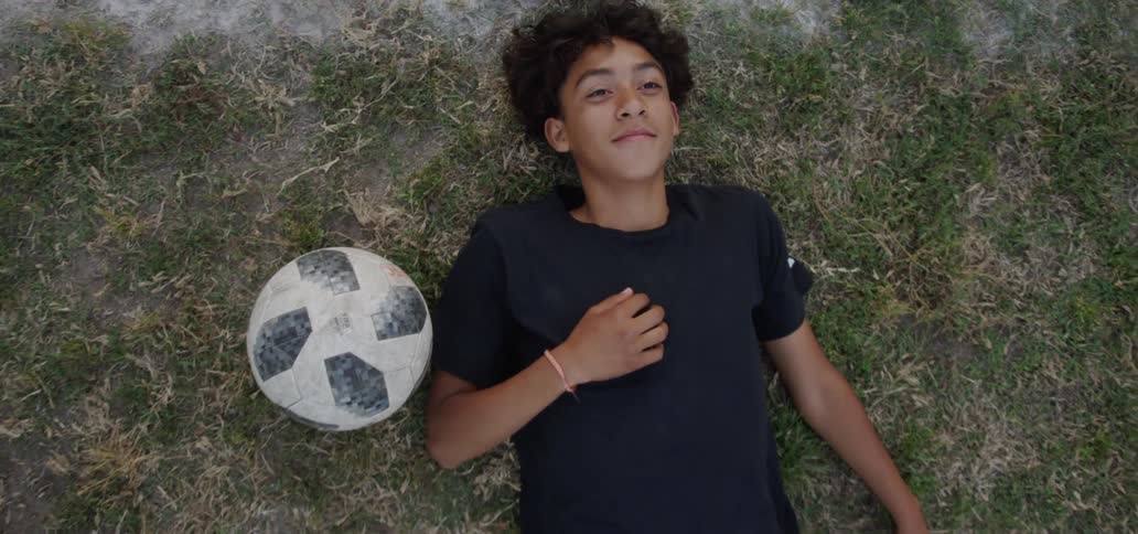 A boy smiles while laying in the grass next to a soccer ball