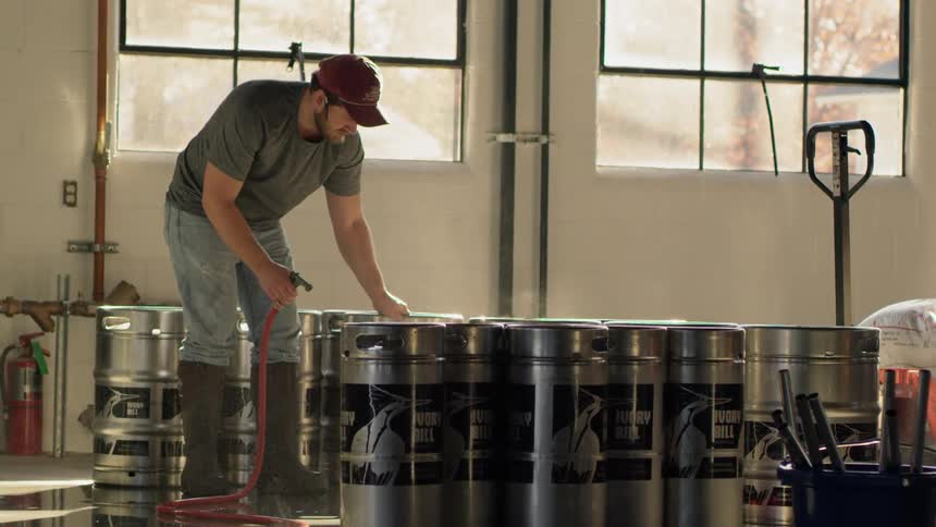 A man is working spraying kegs in a brewery