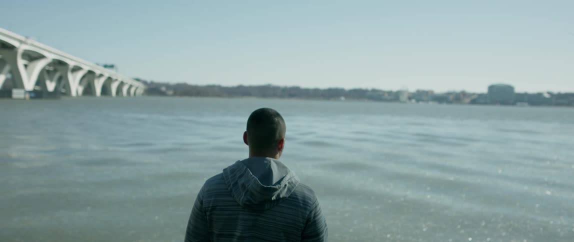 A man stands by the shore near the bridge