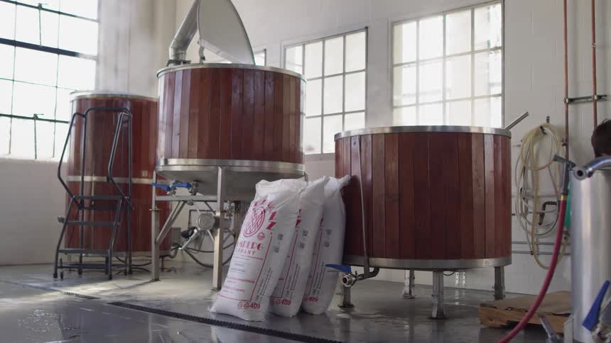 Man carries bags of ingredients next to steaming vats in a factory