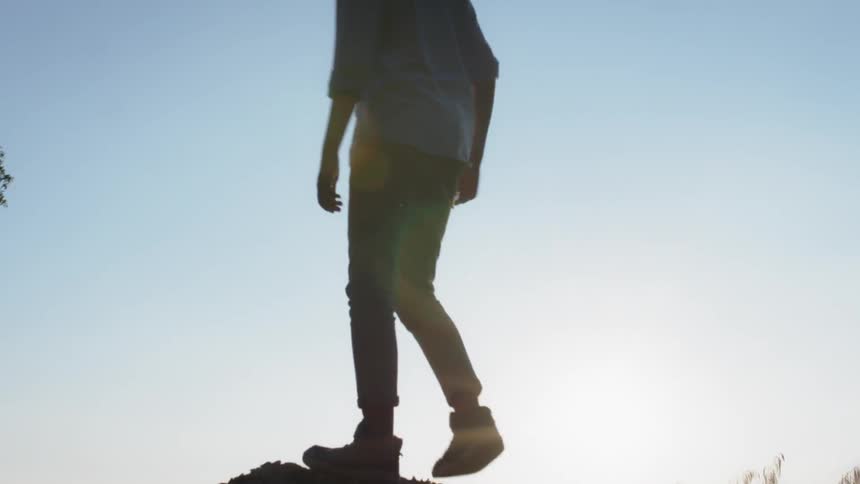 Man walks onto a hill under a blue sky