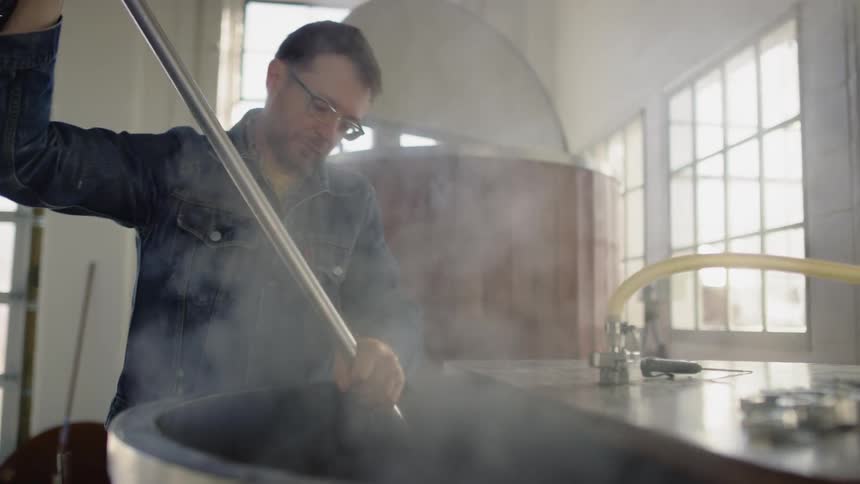 A man is stirring a vat in a brewery in daylight