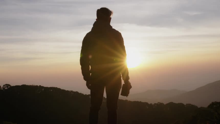 A man stands on a hill watching the sunset