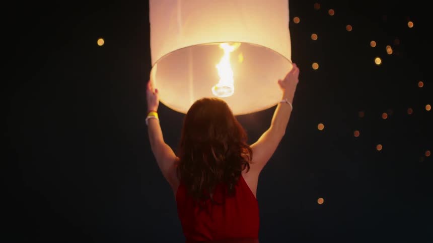 A woman holds a paper lantern up into the night sky