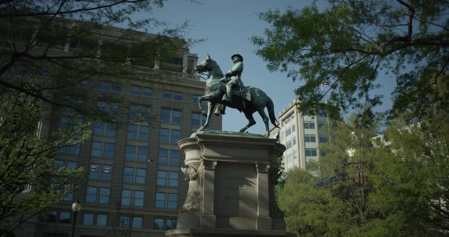Statue of a person riding a horse near buildings and trees