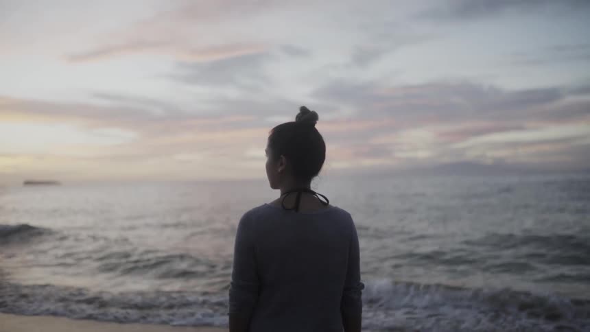 Woman with her hair in a bun standing on a beach with some clouds in the distance