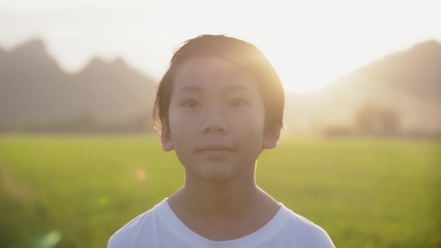 A child stands on a long field as the sun sets
