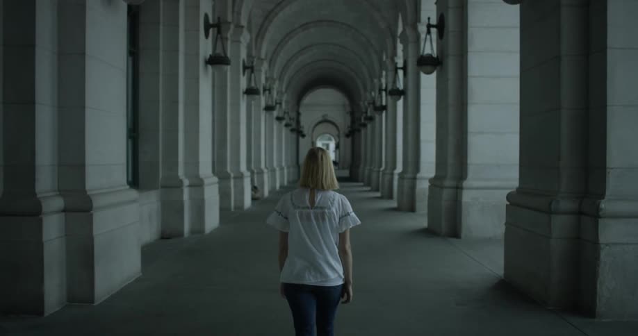 A woman is walking under stone arches of a building