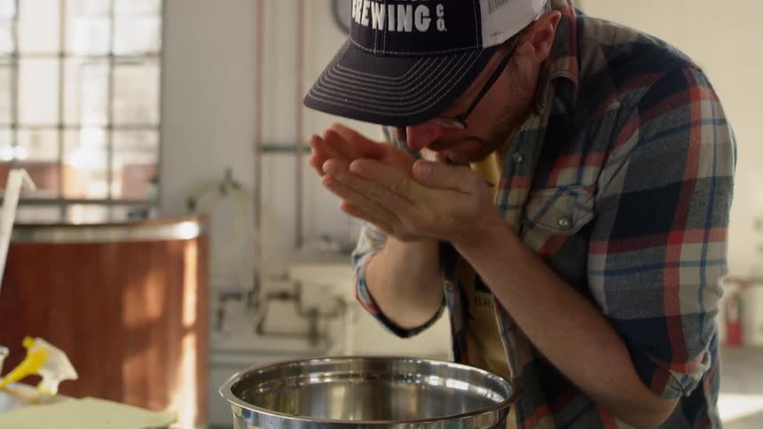 A man adds ingredients to a metal bowl in a brewery