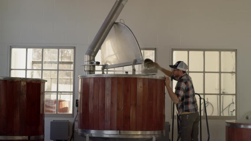 A man skims the top of a barrel in a brewery