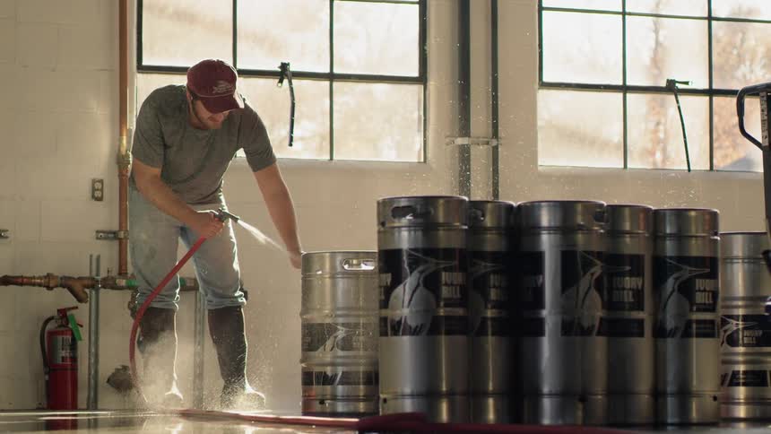 Man uses a hose to rinse off silver containers