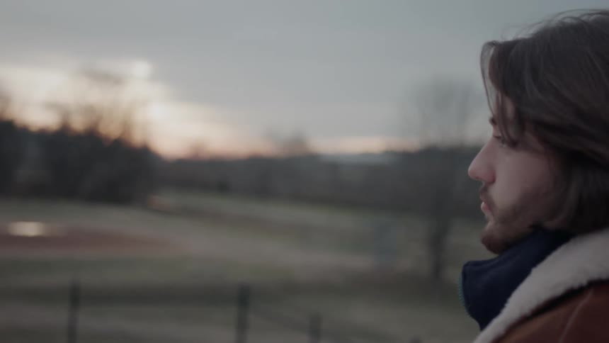 A man is looking at over the field at sunset
