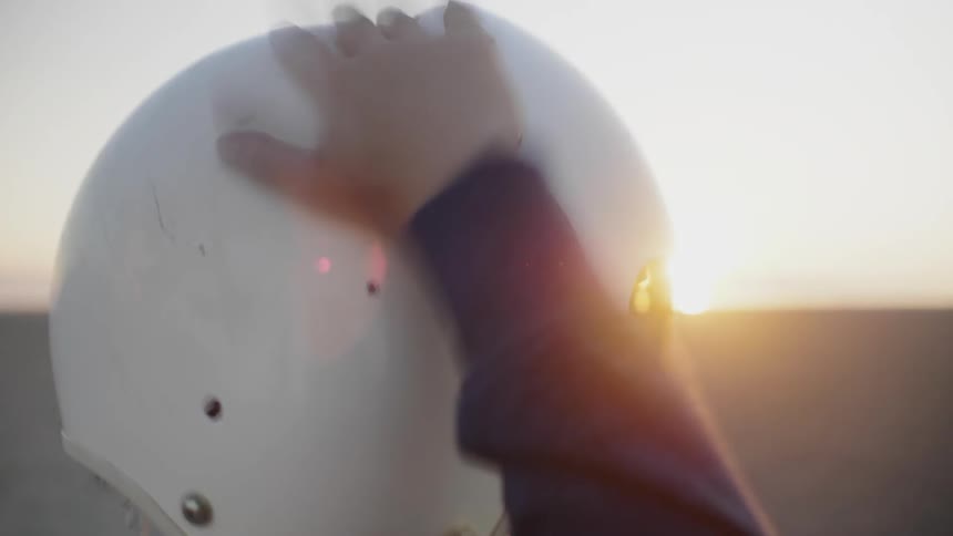 A child taps his helmet at sunset
