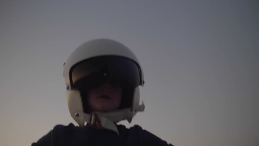 A young boy runs with his arms out while wearing a helmet