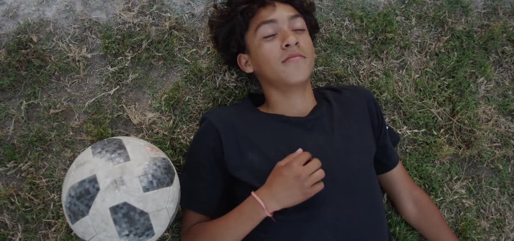A young boy lays in the grass with a soccer ball