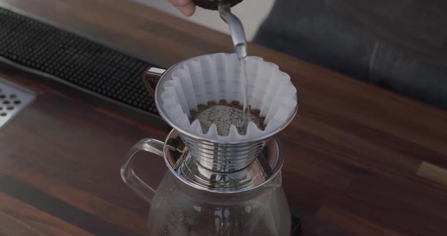 A person pours hot water over a filter full of coffee ground