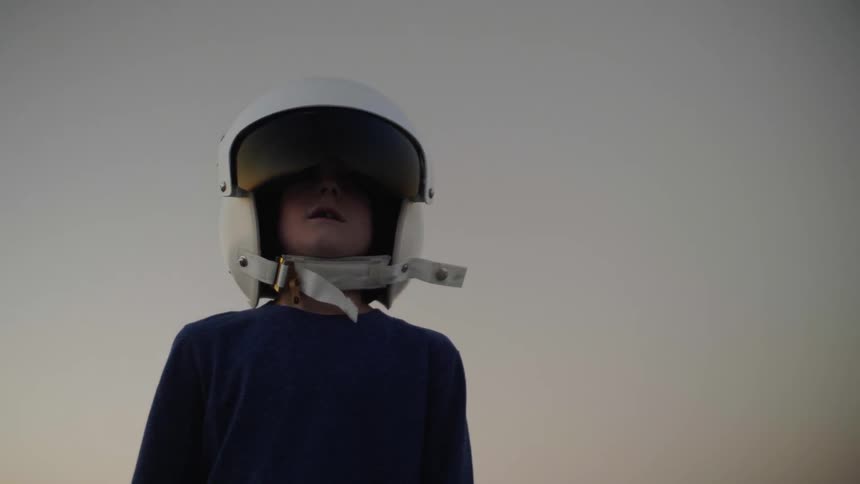 A boy wearing a helmet stands still as the camera moves around him