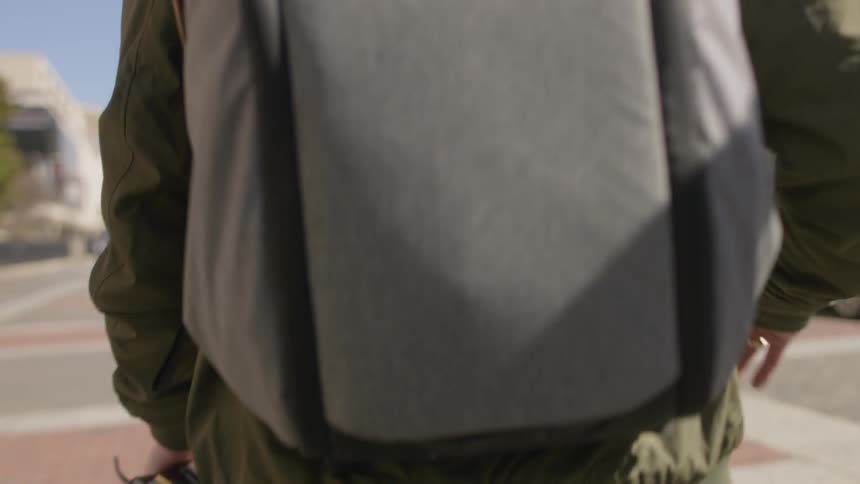 Man carrying a book walks across a city square wearing a backpack