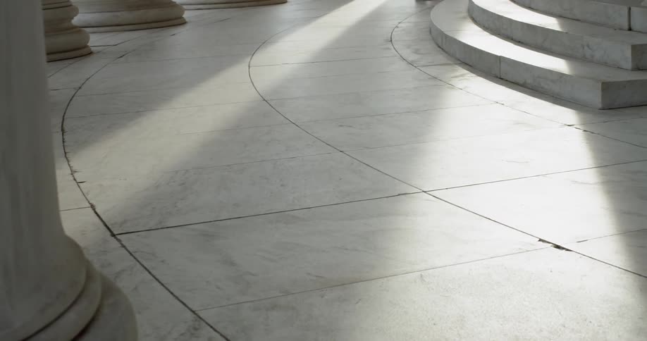 Sunlight spills onto stone floor of Jefferson Memorial between pillars in Washington DC