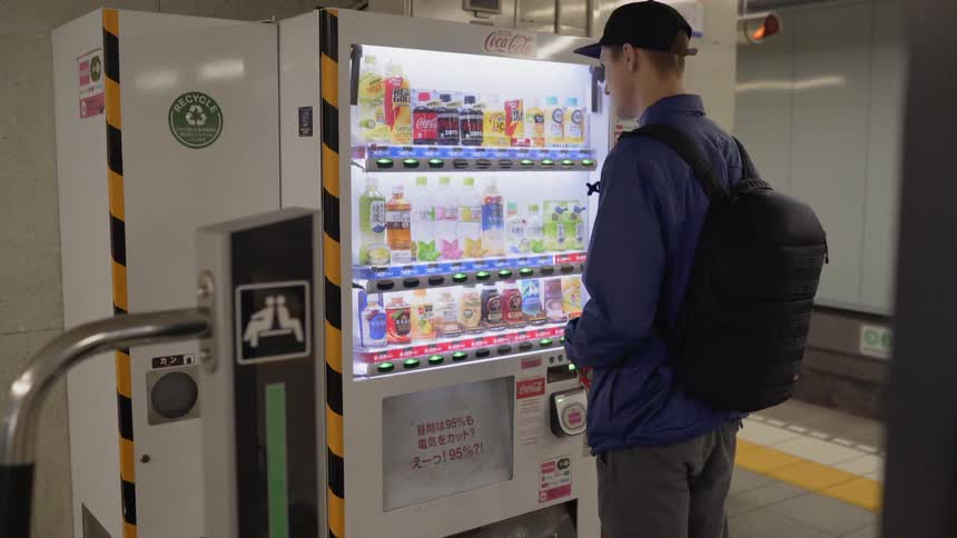 A young man makes a purchase at a Japanese vending machine in the train station