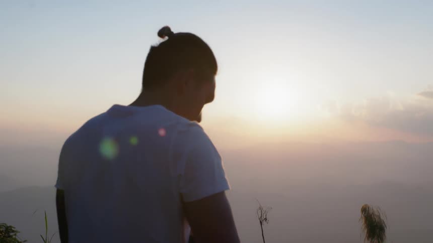 A man stands atop a hill looking at the sun