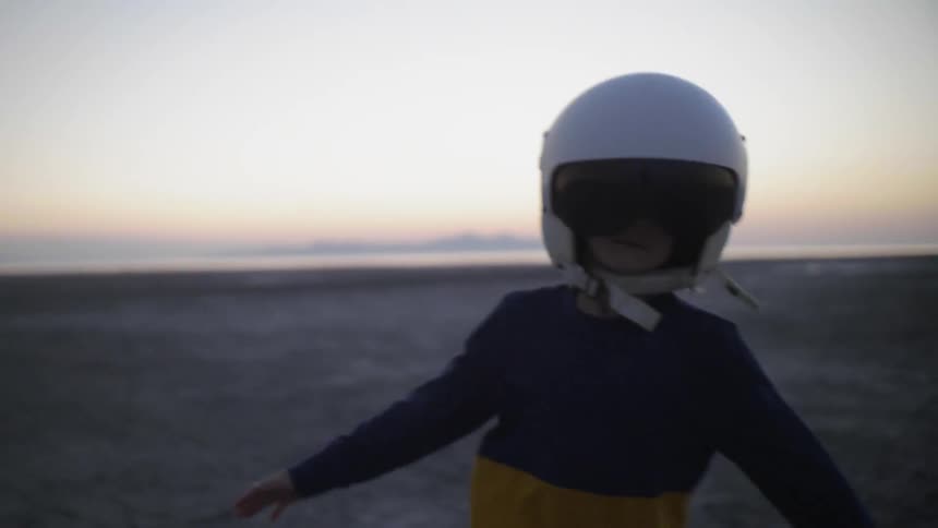 Young child wearing a helmet runs through the flat barren landscape at dusk