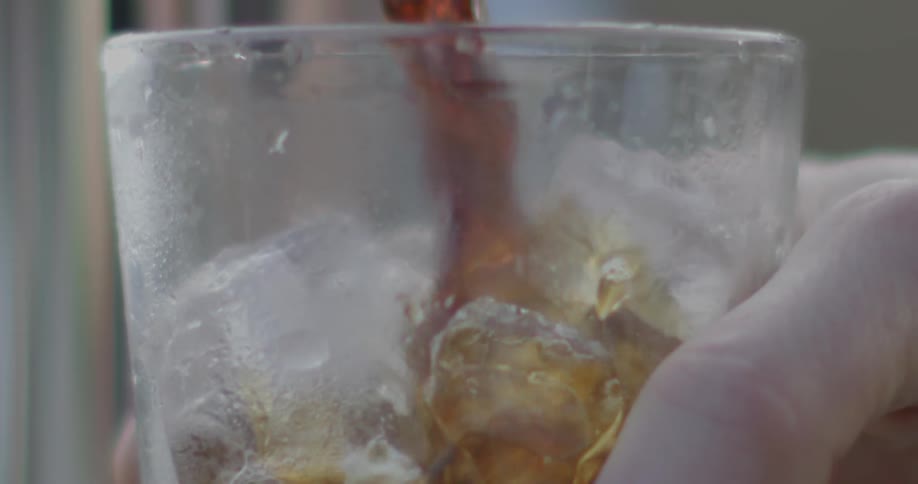 Brown liquid pours into a frosted glass full of ice cubes