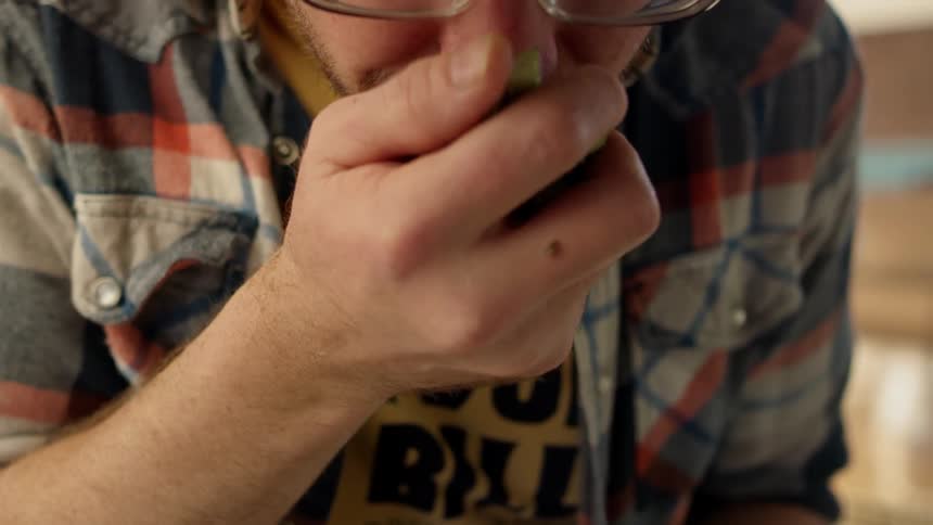 A man is handling and smelling hops inside in daylight