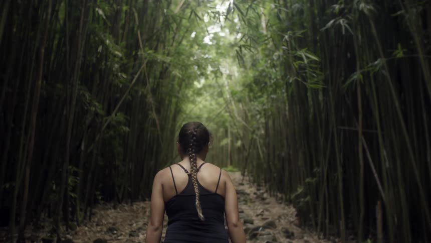 Woman with a braided ponytail walking through a forest trail