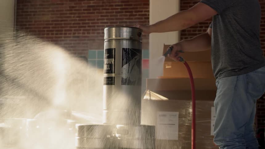 A man hoses off a tank in a brewery