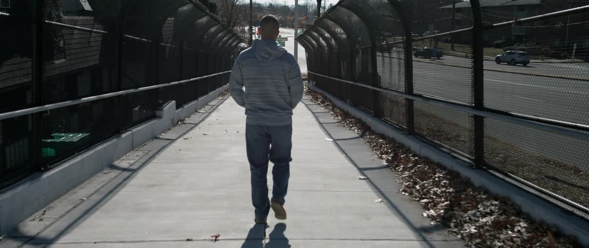 A man is walking on a pedestrian bridge in daylight