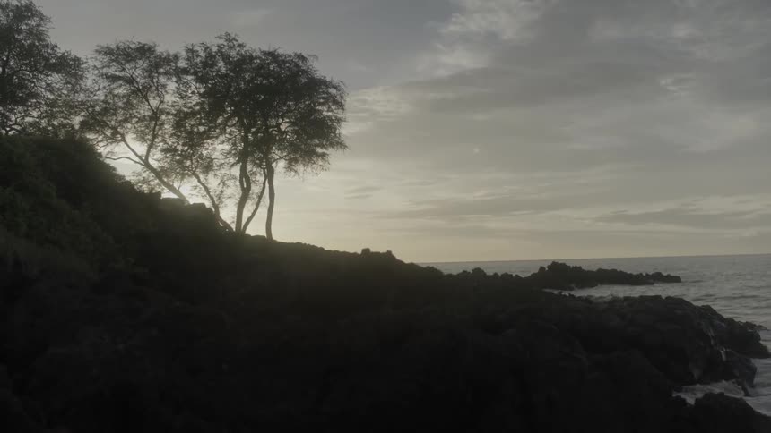 The sun is setting behind a rocky shoreline