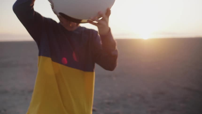 Young boy walks carrying a white helmet then puts it on