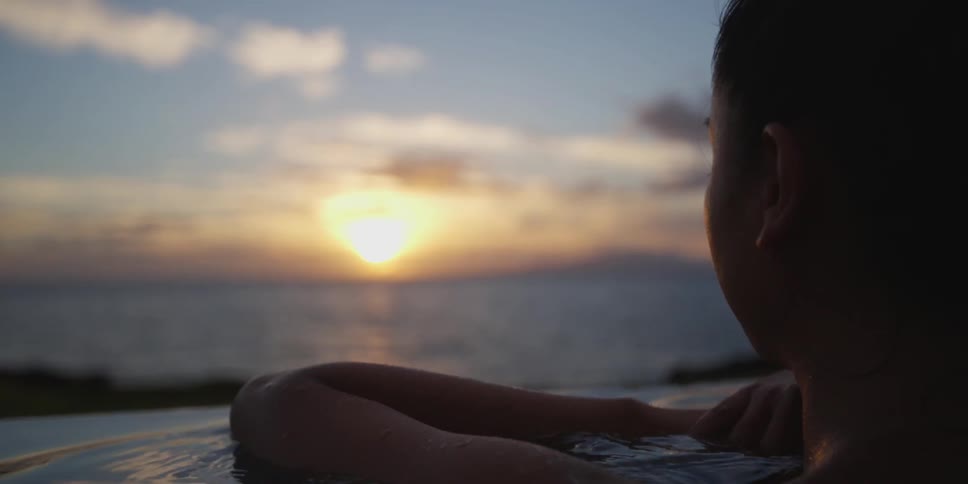 A white woman floats in a pool on the coastline of an ocean