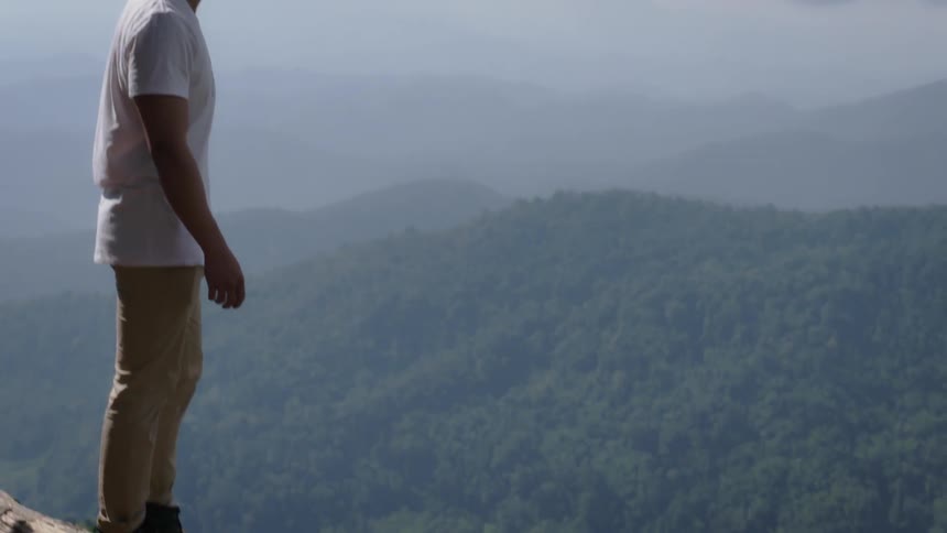 A man stands on the very edge of a mountain top