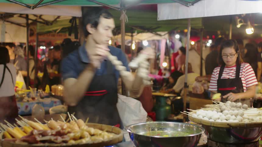 A man and woman cook food at an outdoor market