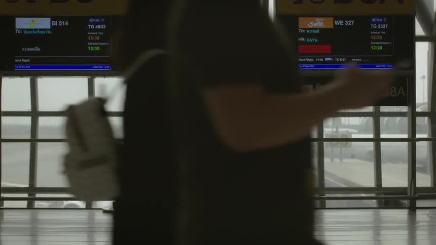 A person stands by the window in a terminal near a suitcase
