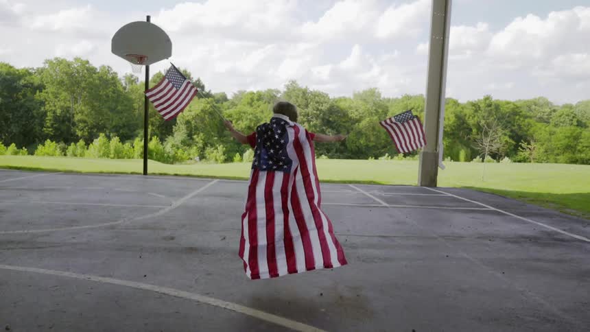 A child wearing a flag as a cap runs across a playground holding two flags